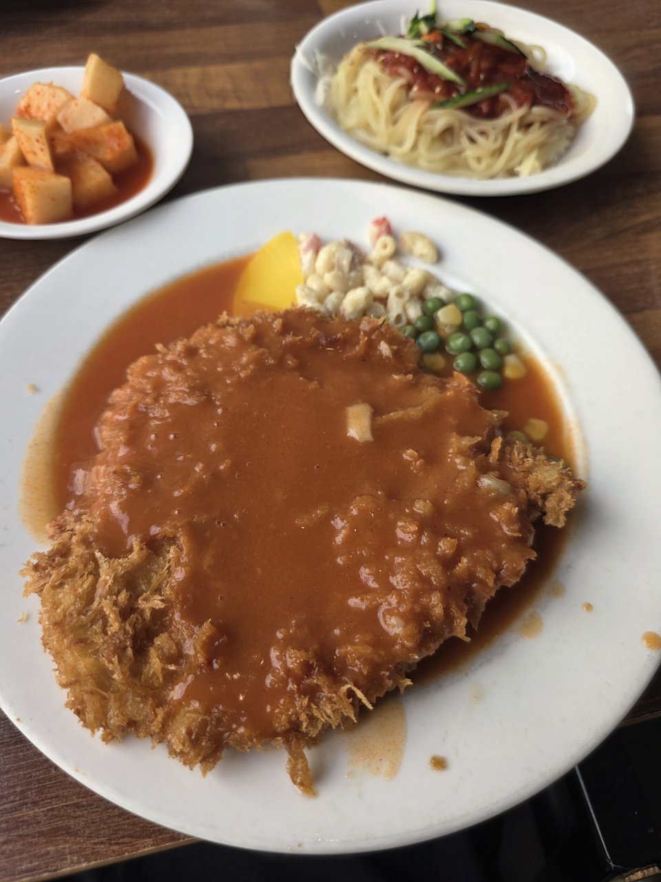 주황빛 소스를 듬뿍 부은 옛날 돈까스와 마카로니, 완두콩, 깍두기와 빨간 양념 면이 놓인 테이블
