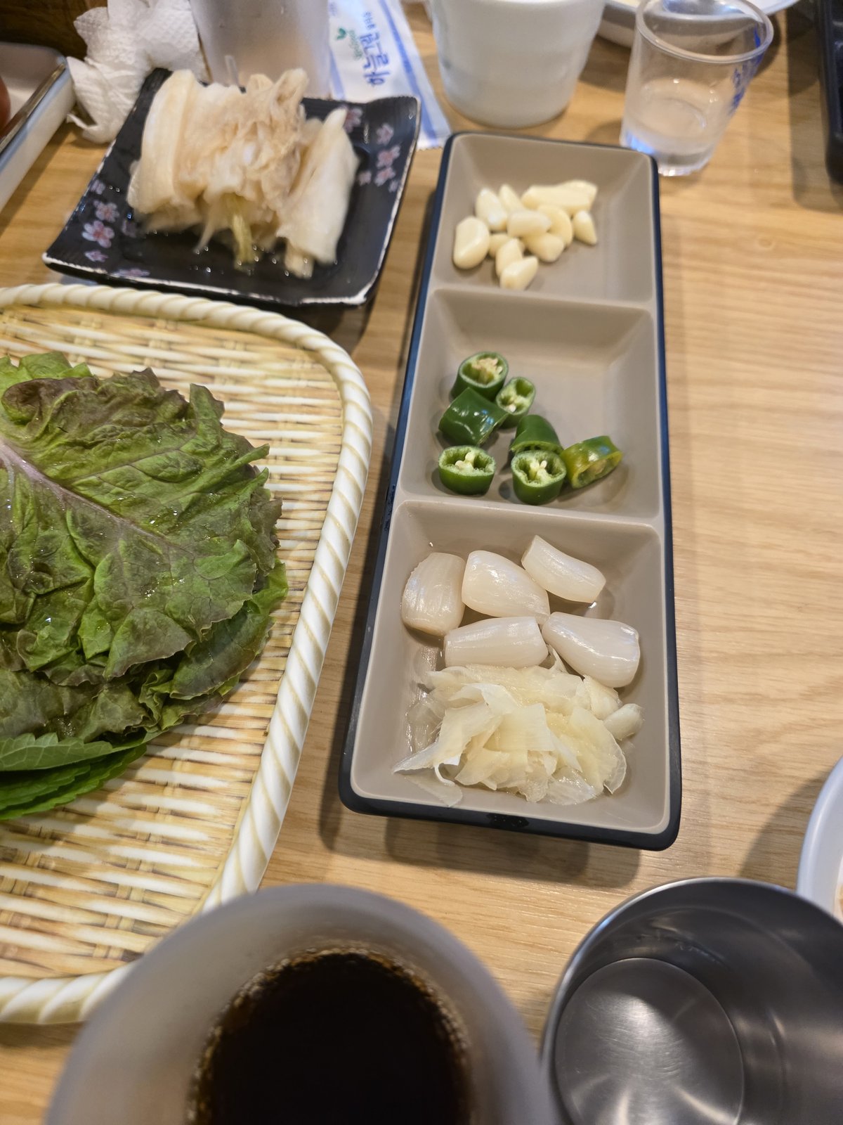 바구니에 담긴 상추와 깻잎 옆으로 마늘과 풋고추 염교가 칸칸이 나뉜 흰 접시에 놓여 있다