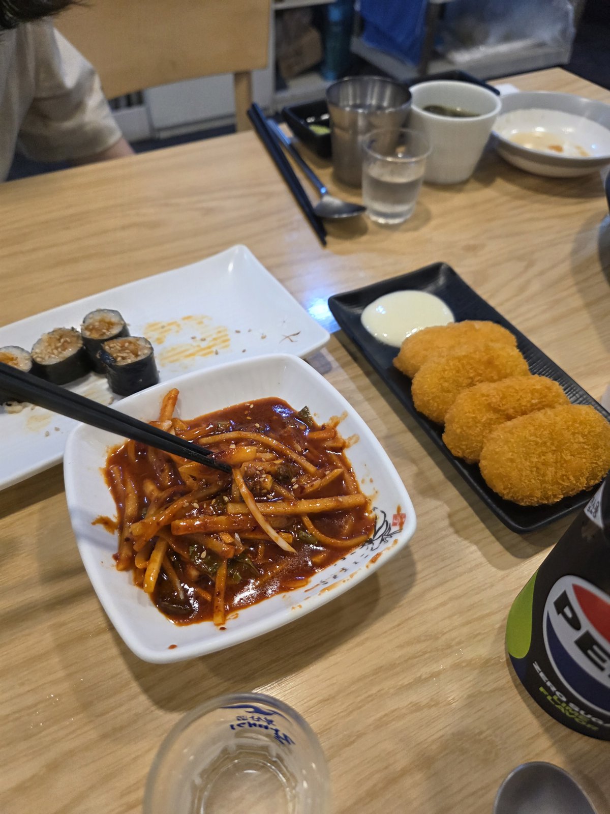 마무리로 나온 매콤한 빨간 양념 면요리와 김밥 고로케가 나무 테이블 위에 놓여 있다