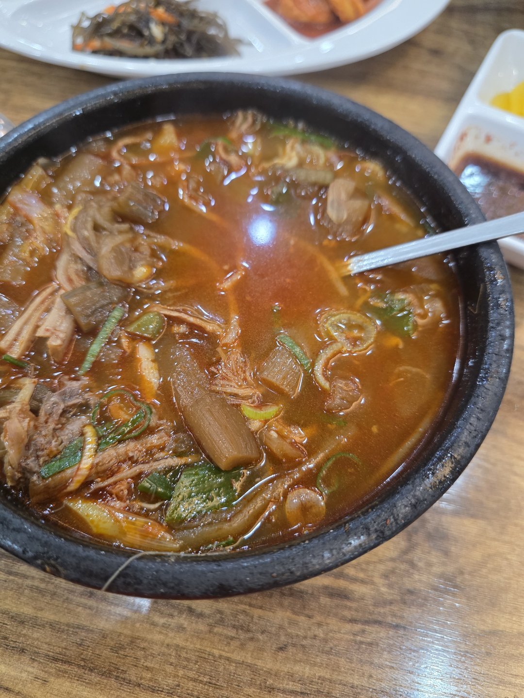 검은 뚝배기에 담긴 육개장과 뒤쪽 반찬 접시
