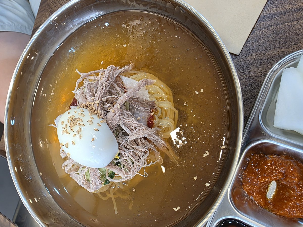 살얼음 육수에 삶은 계란 반쪽과 편육을 올린 부산식 밀면 한 그릇과 옆에 놓인 무절임, 양념장