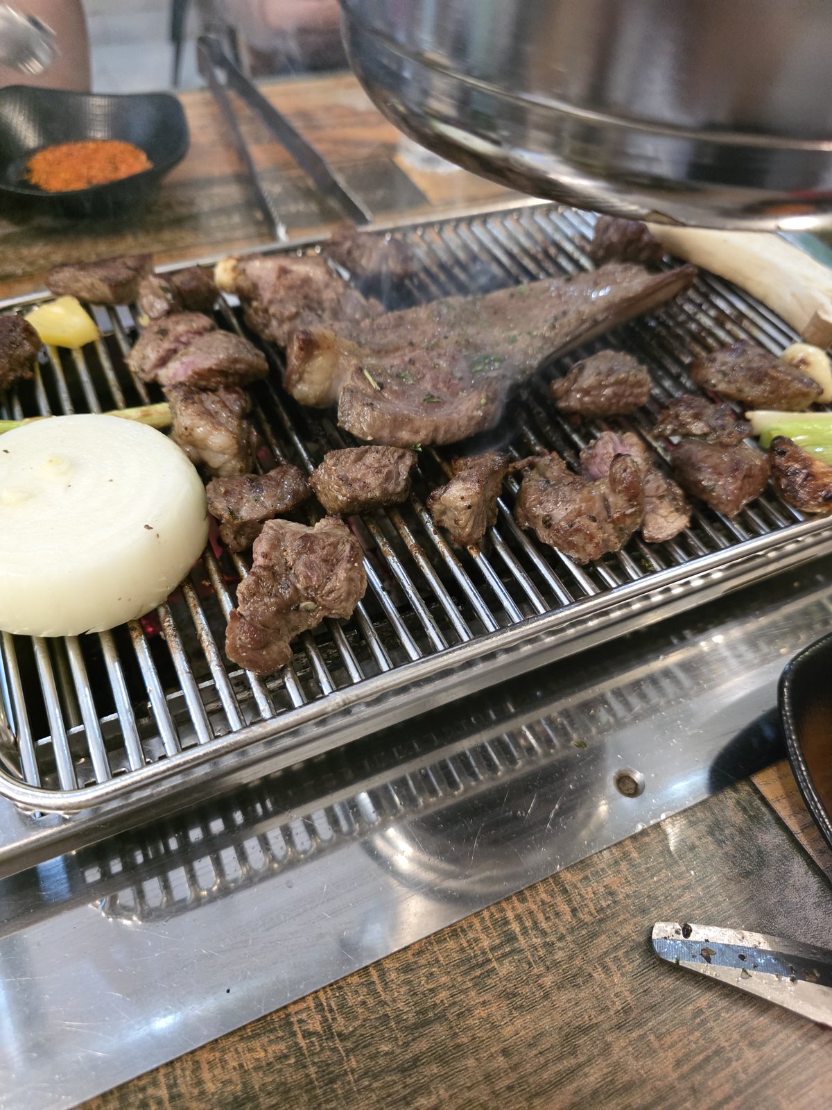스테인리스 석쇠 위에 양갈비 한 대와 깍둑 썬 양고기가 익고 있고 옆에 두툼하게 썬 통양파와 대파가 함께 올라가 있다