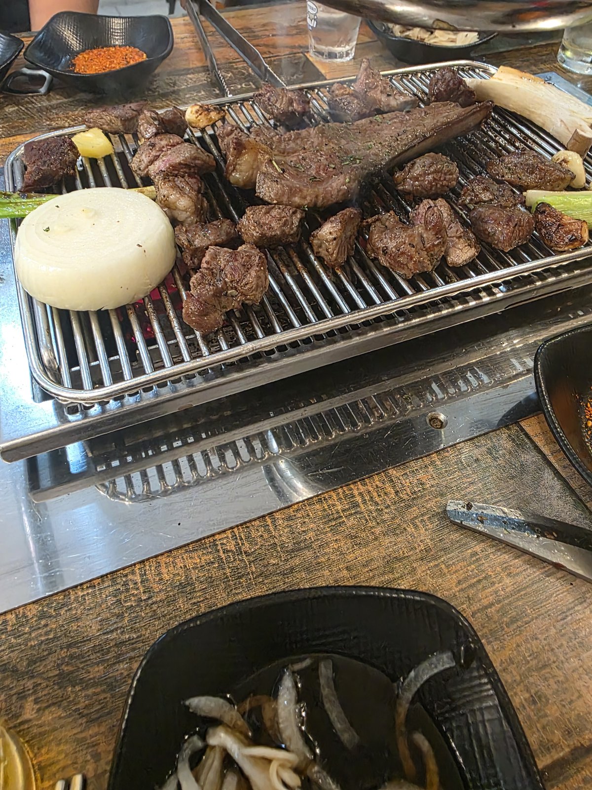 석쇠 가득 구워진 양고기 조각들과 가운데 놓인 두툼한 양갈비, 옆에 통양파와 붉은 양념 종지가 보인다
